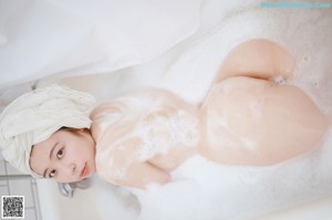 A naked woman sitting in a bathtub with a towel on her head.