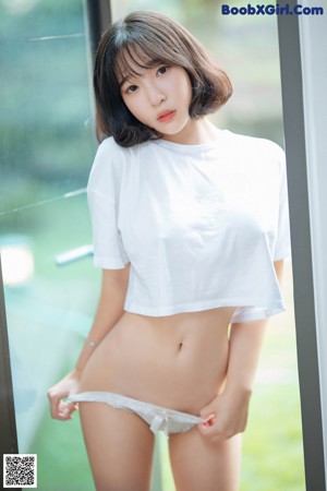 A woman in a white shirt and panties leaning against a window.