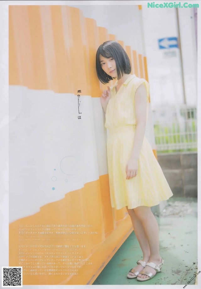 A woman in a yellow dress leaning against a wall.