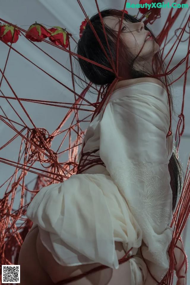 A woman in a white dress is surrounded by red strings.