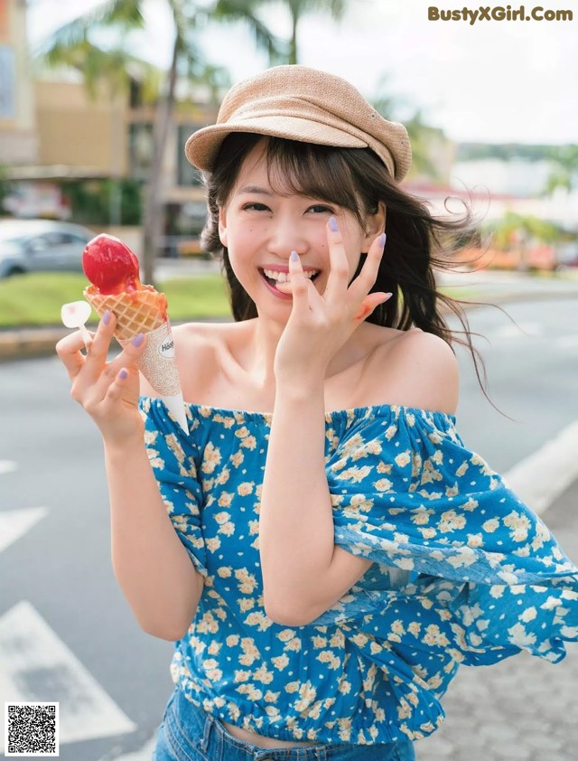 A woman in a blue top and hat holding an ice cream cone.