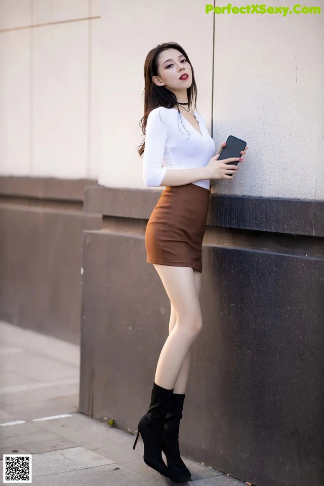 A woman leaning against a wall holding a cell phone.