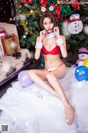 A woman in a red bikini sitting on a bed next to a Christmas tree.