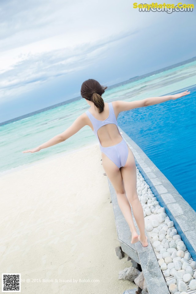 A woman in a blue swimsuit standing on the edge of a swimming pool.