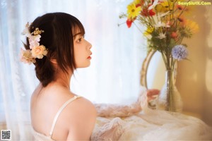 A woman in a wedding dress sitting on the floor with flowers.