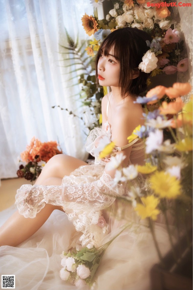 A woman in a white dress sitting on a bed of flowers.