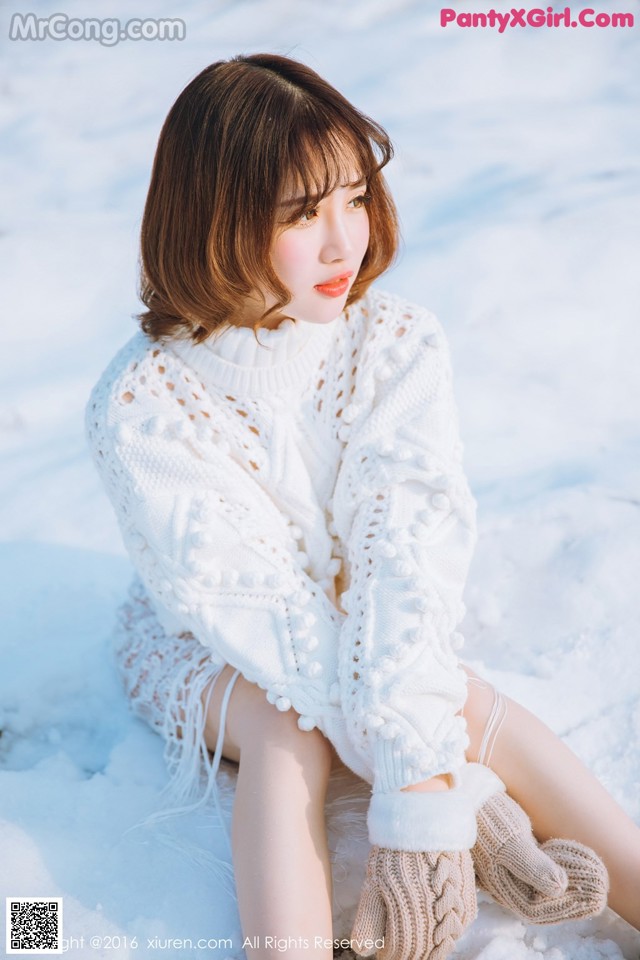 A woman sitting in the snow wearing a white sweater and gloves.