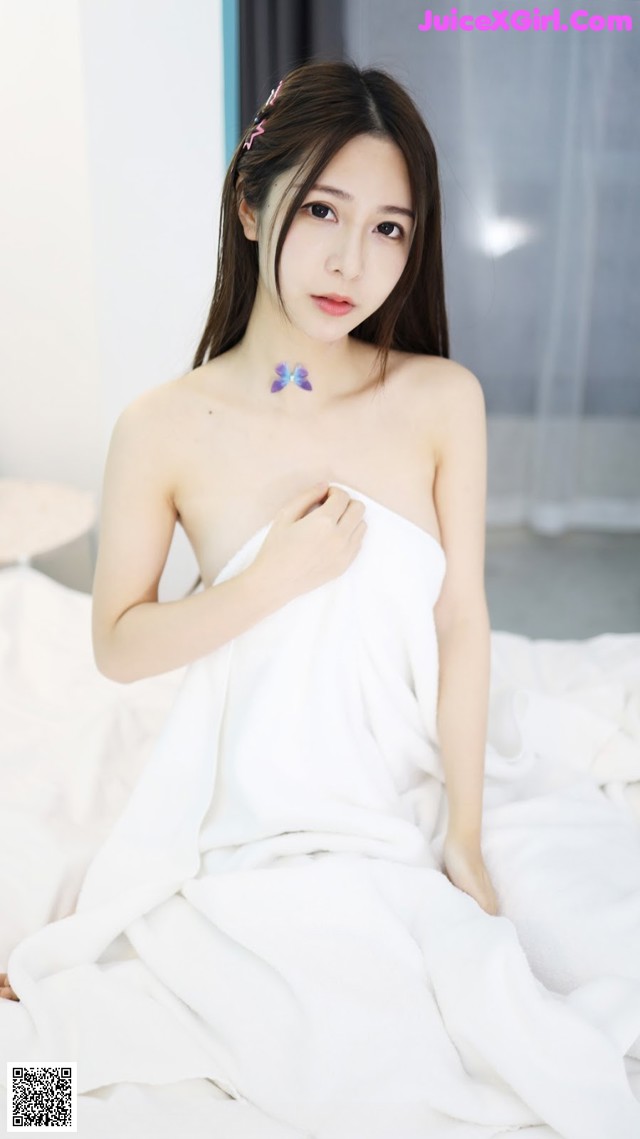 A woman in a white towel sitting on a bed.