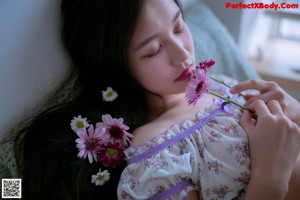 A woman sitting on a bed holding a flower.