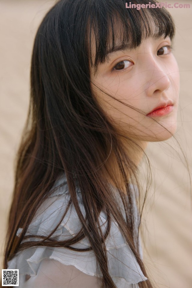 A woman with long brown hair standing in the sand.