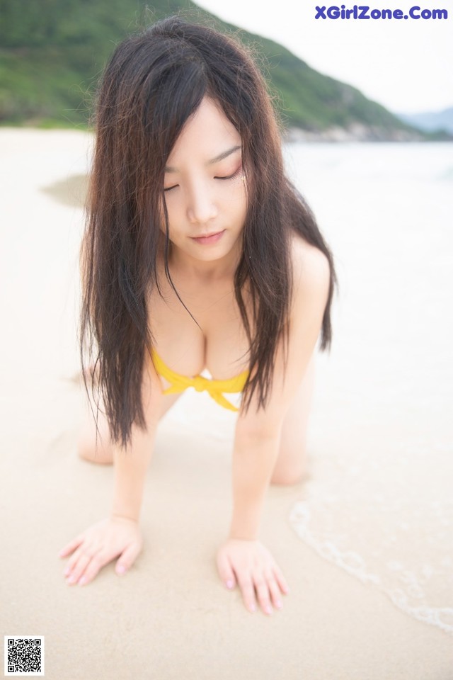 A woman in a yellow bikini laying on the beach.