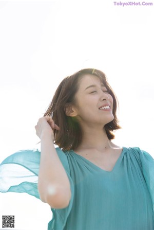 A woman standing in front of a white wall wearing a blue sweater.