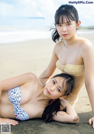 A couple of young women standing next to each other near a pool.