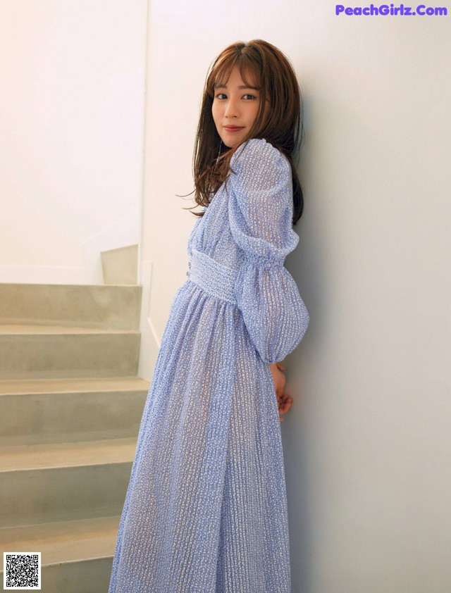 A woman in a blue dress leaning against a wall.