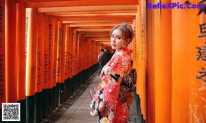 A woman in a kimono standing in front of a torii gate.