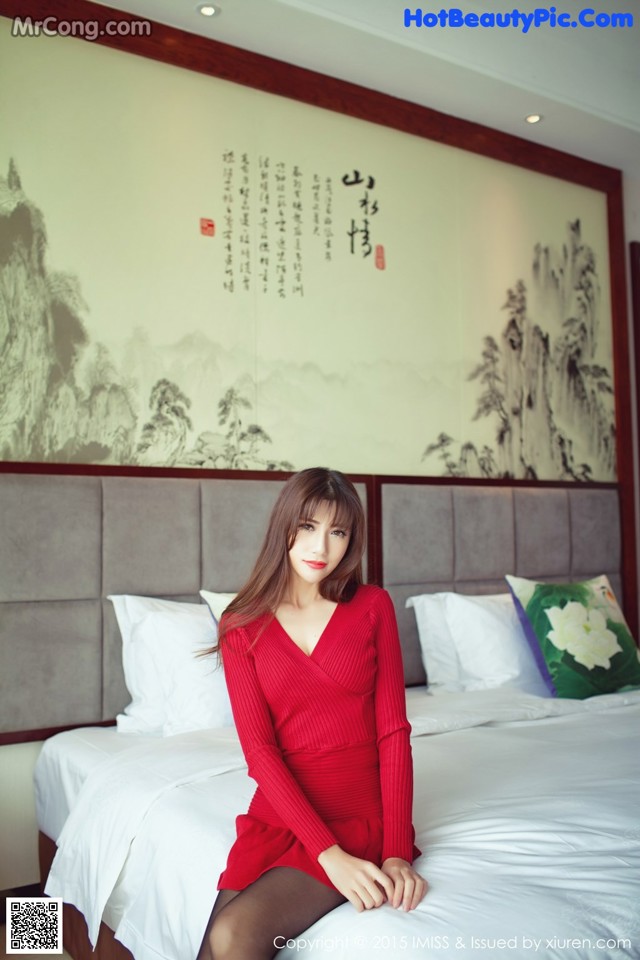 A woman in a red dress sitting on a bed.