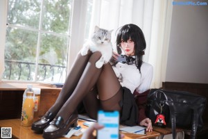 A woman sitting on top of a desk next to a window.