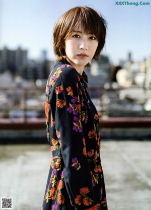 A woman in a black floral dress leaning against a wall.