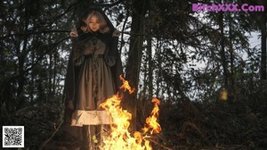 A woman sitting in front of a fire in the woods.