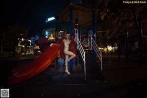 A naked woman sitting on a chair in front of a lamp.