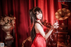 A woman in a red dress sitting on a chair holding a glass of wine.