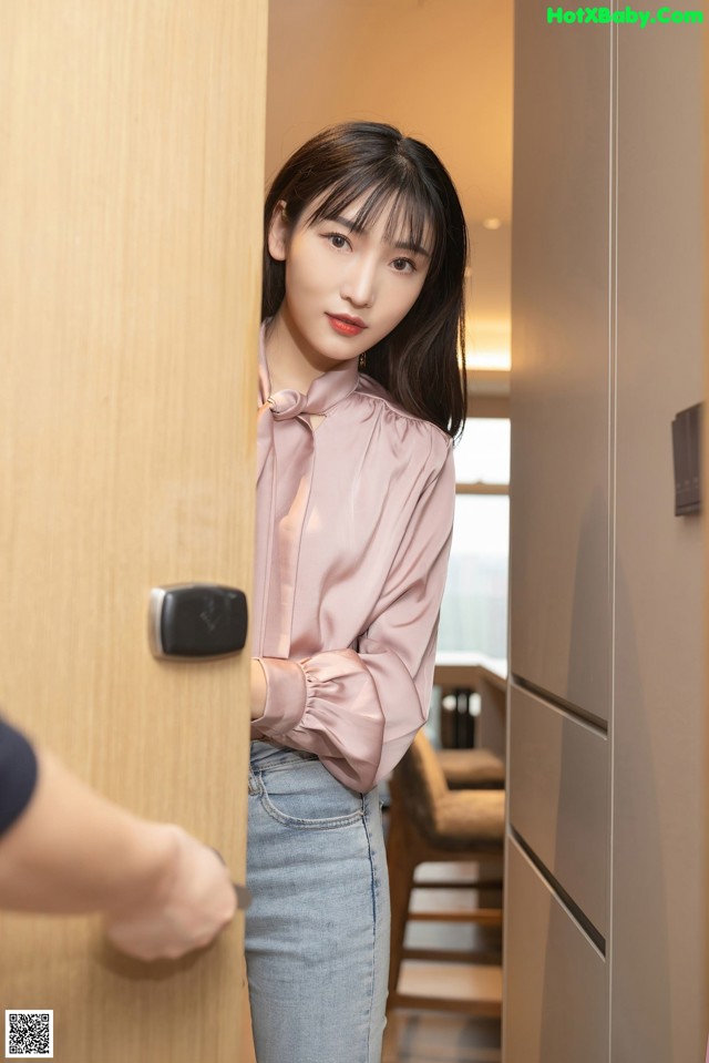 A woman standing in front of a door with her hand on the door handle.