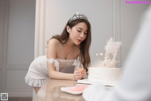 A woman in a white dress standing next to a table with a cake.