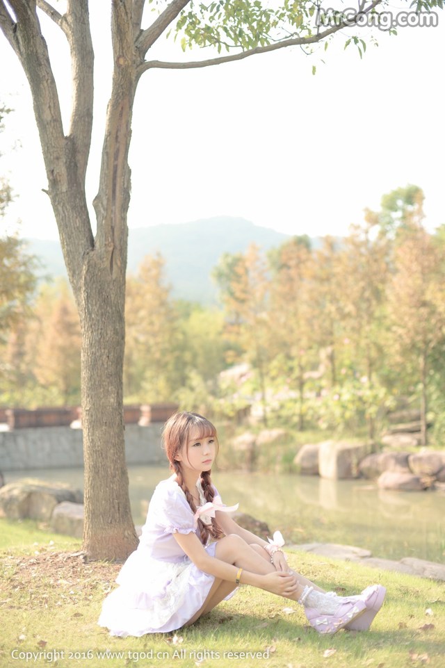 A woman in a white dress sitting under a tree.